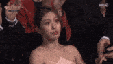 a woman in a pink dress is sitting in a crowd of people and making a face .