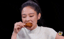 a woman in a white shirt is eating a fried chicken wing .
