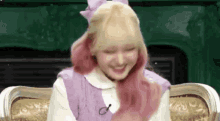 a girl with blonde and pink hair is sitting on a couch .