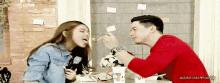 a man and a woman are sitting at a table eating food . the woman is sticking her tongue out at the man .