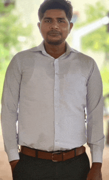 a man wearing a white shirt and black pants is standing with his hands in his pockets