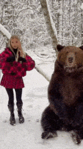 a woman in a red plaid skirt stands next to a bear in the snow