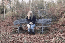 a woman is sitting on a wooden bench in a forest .