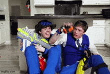 two boys are playing with nerf guns in a kitchen ..