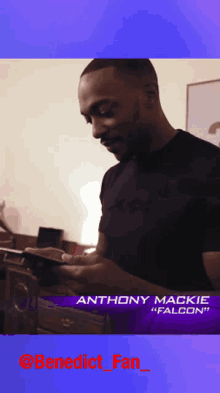 a man in a black shirt is looking at a phone with the name anthony mackie on the bottom