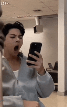 a man is taking a picture of himself in a mirror while yawning while holding a cell phone .