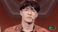 a man wearing glasses and hoop earrings is sitting in front of a microphone with an iy logo on the bottom right