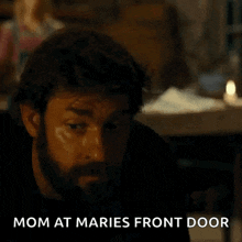 a man with a beard is talking on a cell phone while sitting at a table in a dark room .
