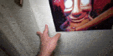 a person 's hand is reaching for a picture of a clown on the wall