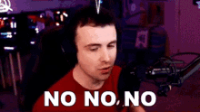 a man wearing headphones and a red shirt is sitting in front of a microphone and says no no no .