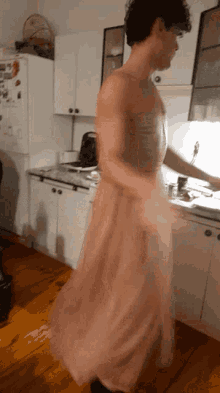a man in a pink dress stands in a kitchen