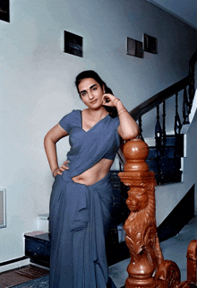 a woman in a blue saree stands in front of a wooden railing