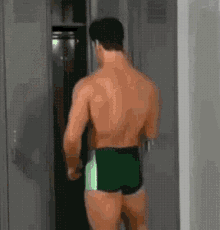 a shirtless man in green swim trunks is walking into a locker room .