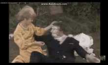 a woman in a yellow dress is putting a pie on a man 's face