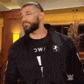 a man with a beard and a black jacket is standing in a room .