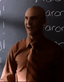 a bald man stands in front of a blackboard with the word aron written on it