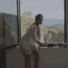 a woman in a white robe stands in front of a window