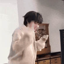 a man in a white sweater is standing in a room holding a remote control .