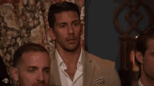 a group of men are standing next to each other in a room . one of the men is wearing a tan suit .