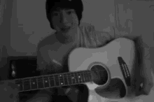 a black and white photo of a young man playing an acoustic guitar