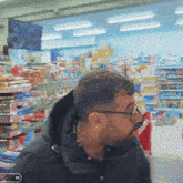 a man wearing glasses and a black jacket is standing in a grocery store