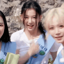 three girls are standing next to each other in front of a rock wall .