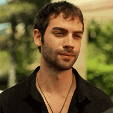 a man with a beard wearing a black shirt and a chain around his neck