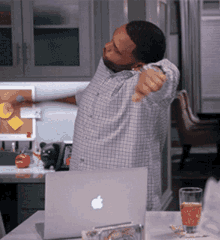 a man in a plaid shirt stretches his arms in front of an apple laptop