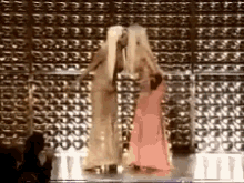 two women are kissing on a stage in front of a wall with a lot of letters on it