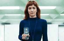 a woman wearing a blue sweater and a lanyard is holding a glass of water .