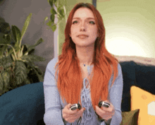 a woman with red hair is sitting on a couch holding a video game controller