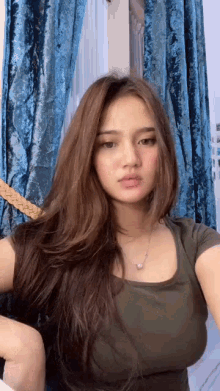 a woman with long brown hair is wearing a green shirt and a necklace .