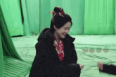 a woman in a black jacket is smiling in front of green curtains