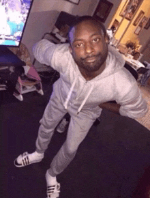 a man in a grey hoodie and sweatpants is posing for a picture in a living room