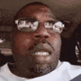 a man wearing glasses and a white shirt is smiling while sitting in a car .