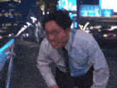 a man in a white shirt and blue tie is walking down a street at night