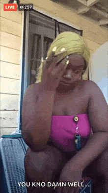 a woman in a pink top is sitting in front of a window and covering her face .