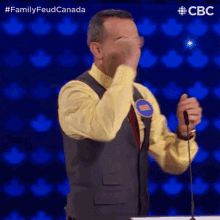 a man covering his face with his hand while standing in front of a microphone on a family feud show