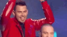 a man in a red jacket is dancing on a stage with his hands in the air .