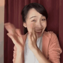 a woman in a pink jacket is smiling and clapping her hands .
