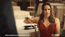 a woman in a red dress sits at a table with a glass of wine and a nbc logo