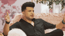 a man in a black shirt sits on a pink couch with his arms outstretched