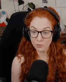 a woman with red hair is wearing headphones and glasses while talking into a microphone .