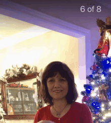 a woman stands in front of a christmas tree with the number 6 of 8 on the ceiling above her