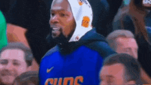 a basketball player wearing a hoodie is sitting in the stands during a basketball game .