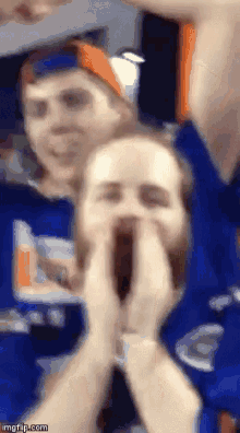 a man and a woman are making a face with their hands in front of their mouths .