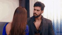 a man in a suit and a woman in a blue blouse are looking at each other .
