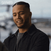 a man in a black jacket is smiling in front of a skymed logo