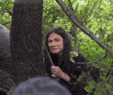 a woman is peeking out from behind a tree in a forest .