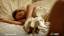 a woman is sleeping in a bed with a nbc logo in the corner